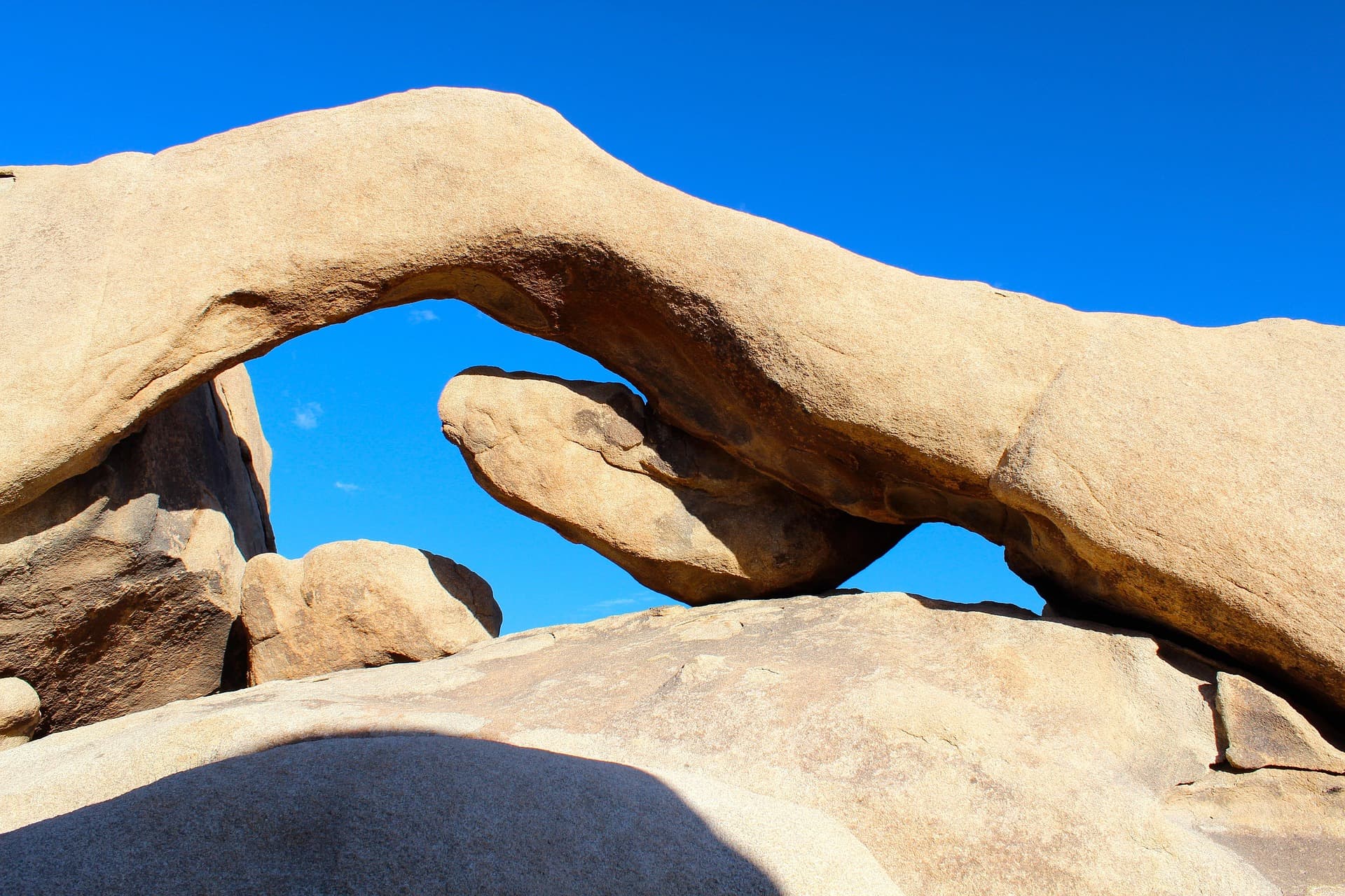 Arch Rock, a granite arch in the Joshua Tree desert, beneath a deep blue sky