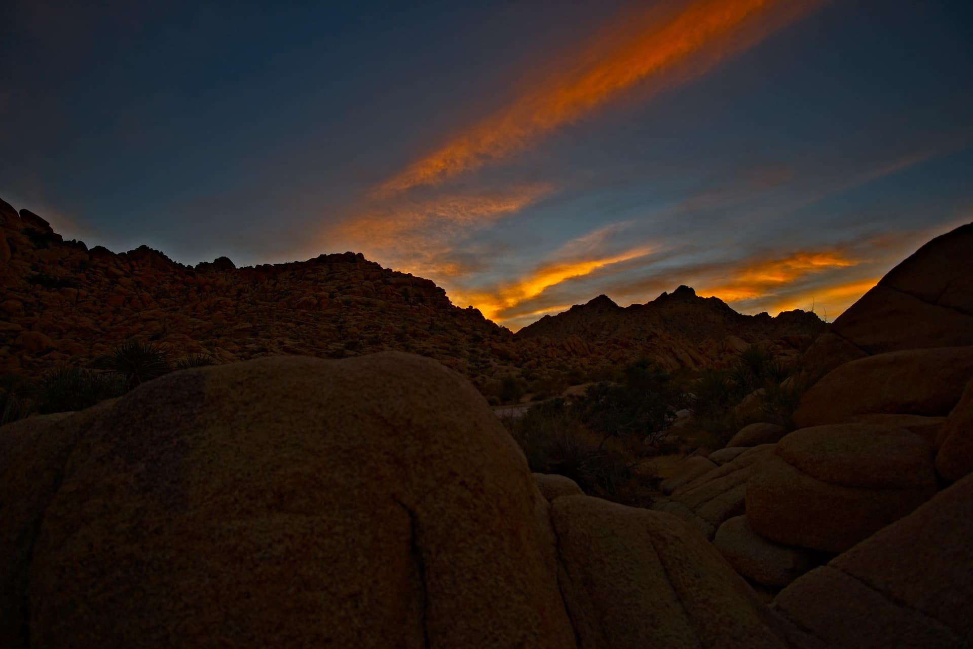 Granite boulder fields in the Joshua Tree desert under a burning sunset sky